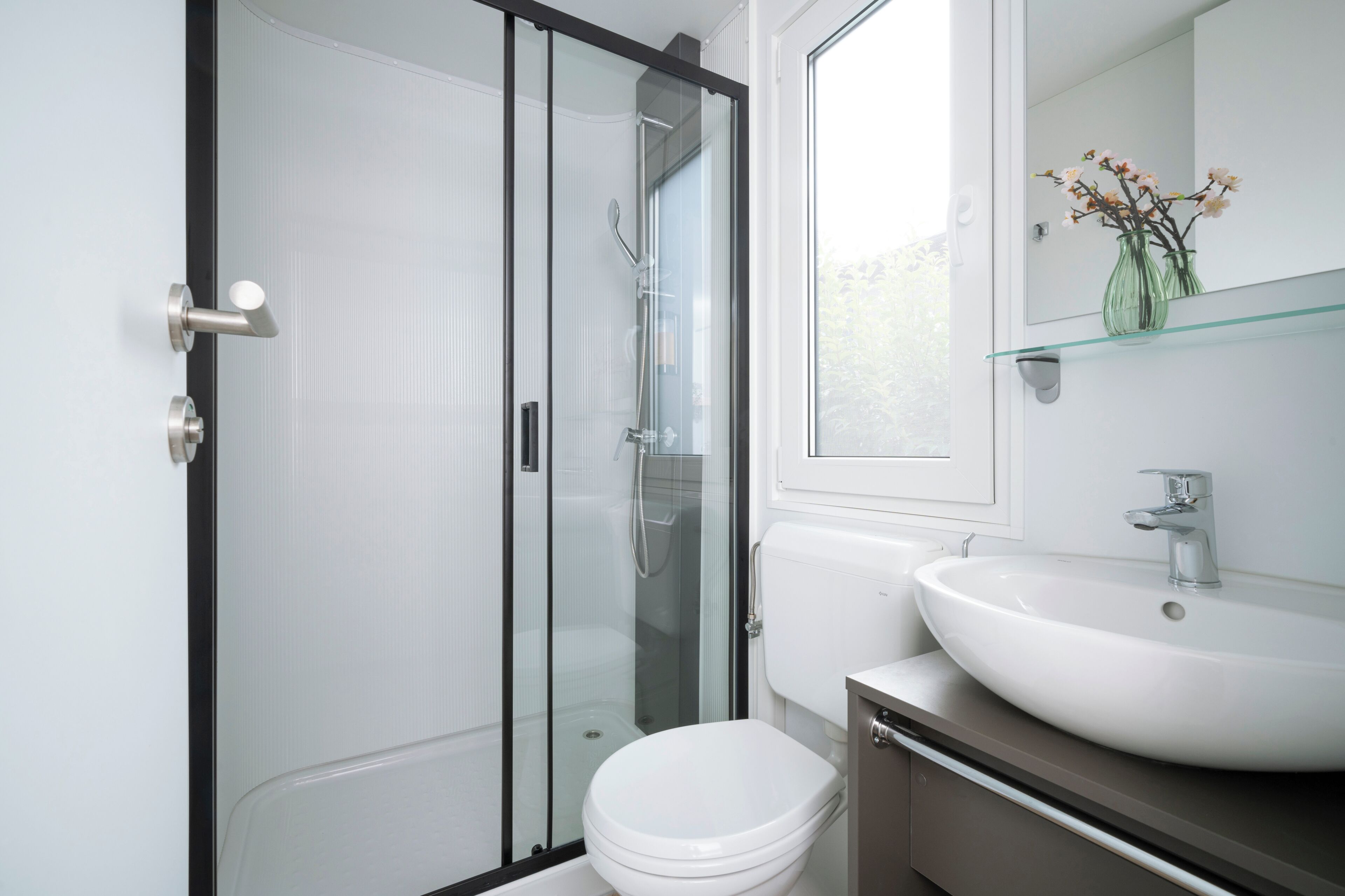 A modern bathroom with a glass-enclosed shower, a white toilet, and a sink with a glass shelf above it.