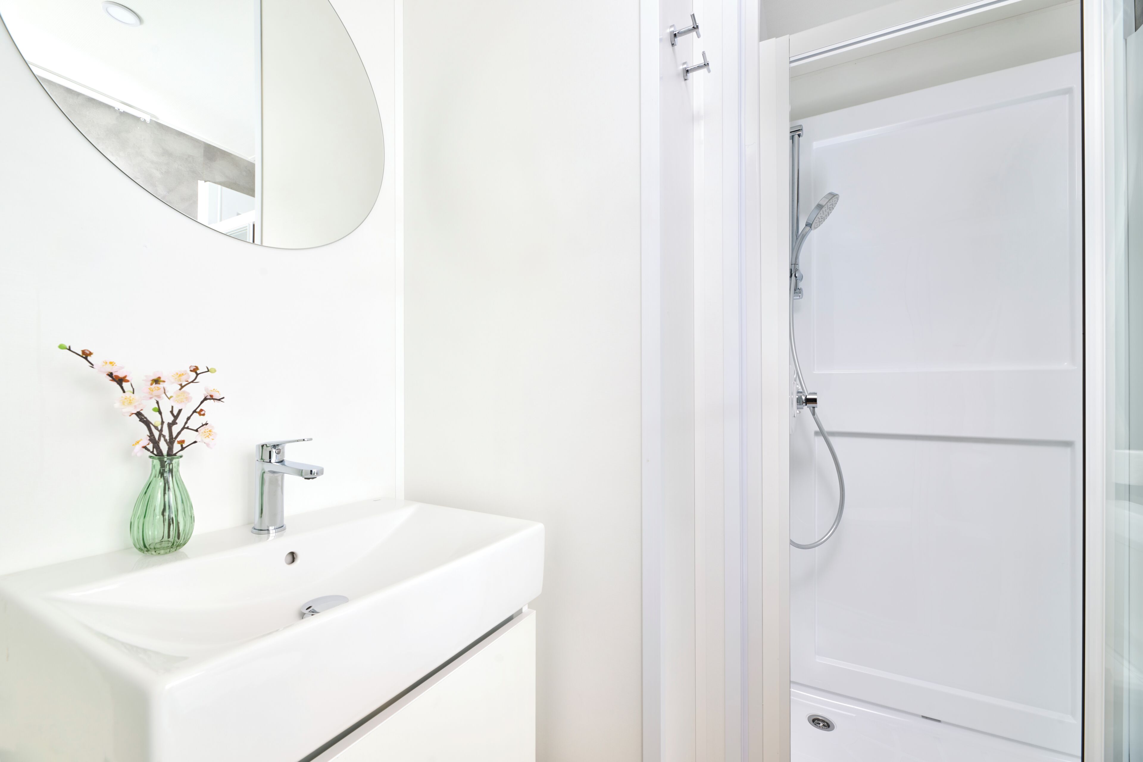 Un baño con lavamanos blanco, espejo y ducha.