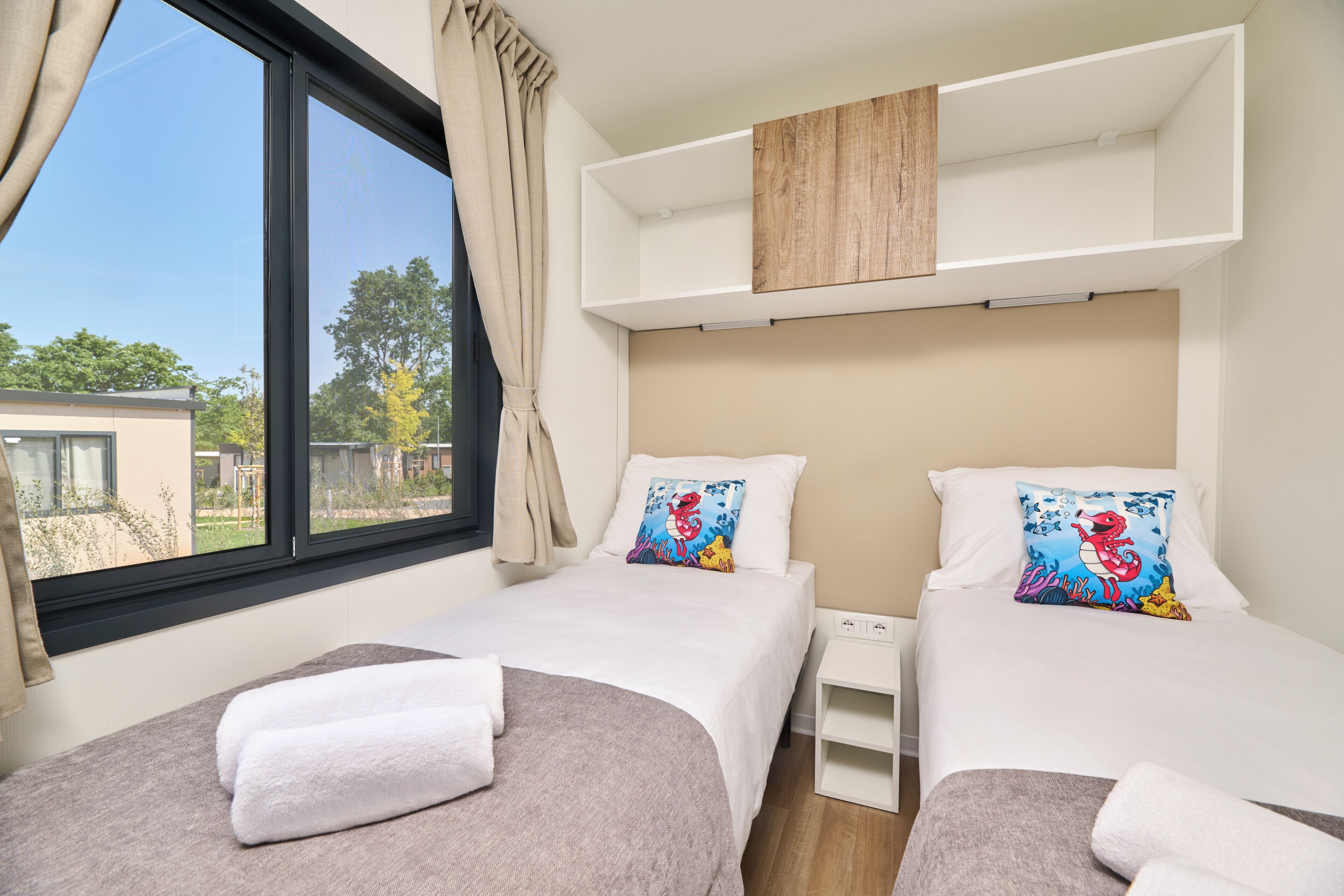 A hotel room with two beds, a window with curtains, and a view of the outside.