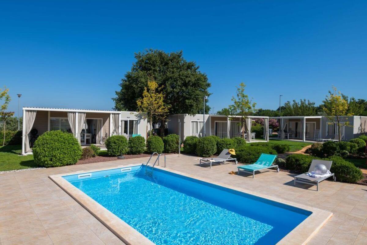 Una piscina con sillas de descanso, un espacio al aire libre cubierto y arbustos bien cuidados.