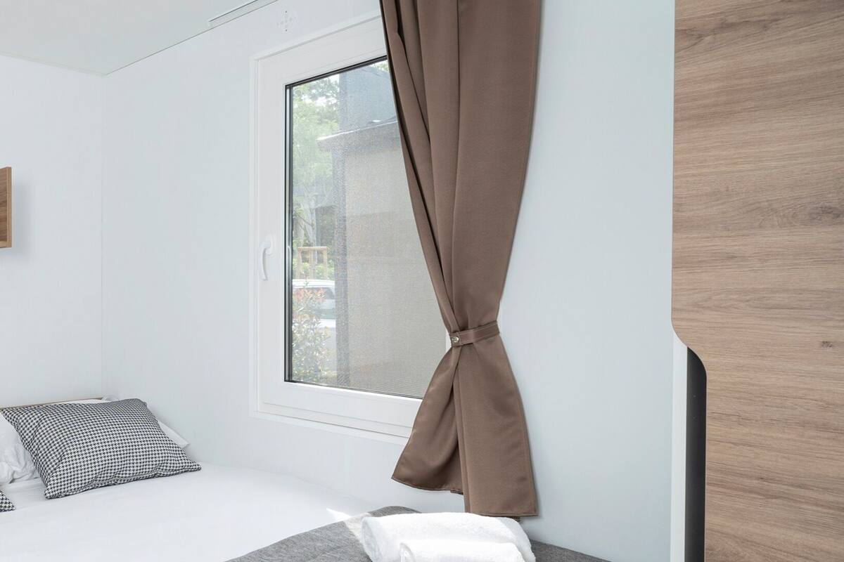 Un dormitorio moderno con cama, ventana con cortinas y un armario de madera.