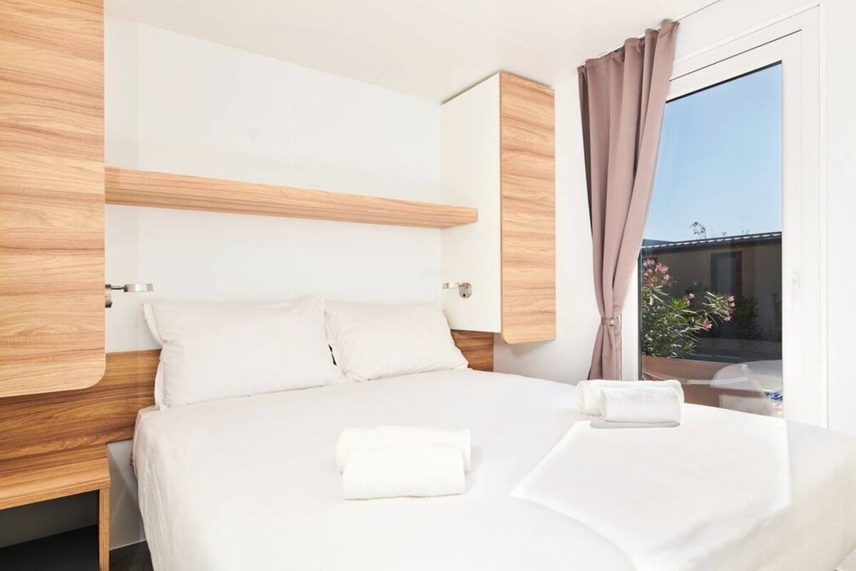 Una habitación de hotel moderna con cabecera de madera, un ventanal con cortinas y una cama bien hecha con toallas.