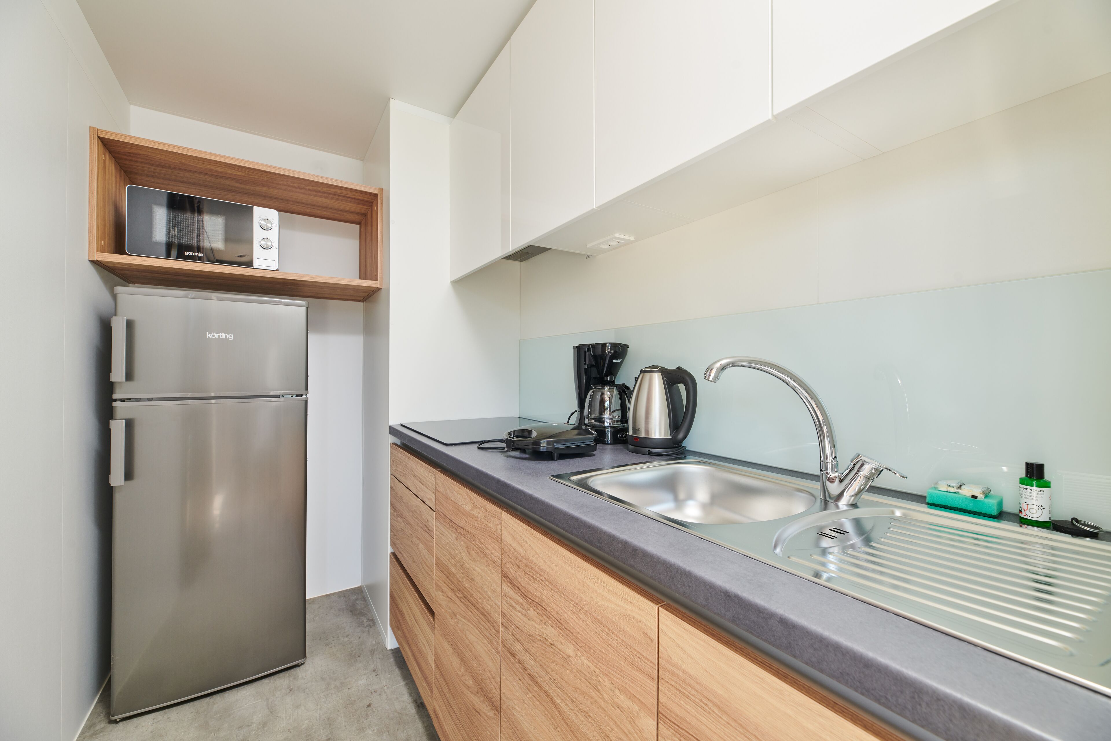 A compact kitchen with a stainless steel refrigerator, a microwave, a coffee maker, and a sink with a faucet.