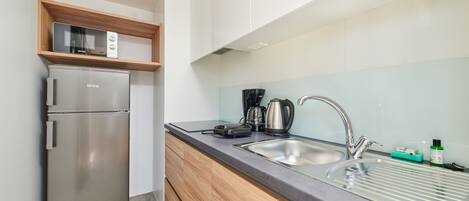 A compact kitchen with a stainless steel refrigerator, a microwave, a coffee maker, and a sink with a faucet.