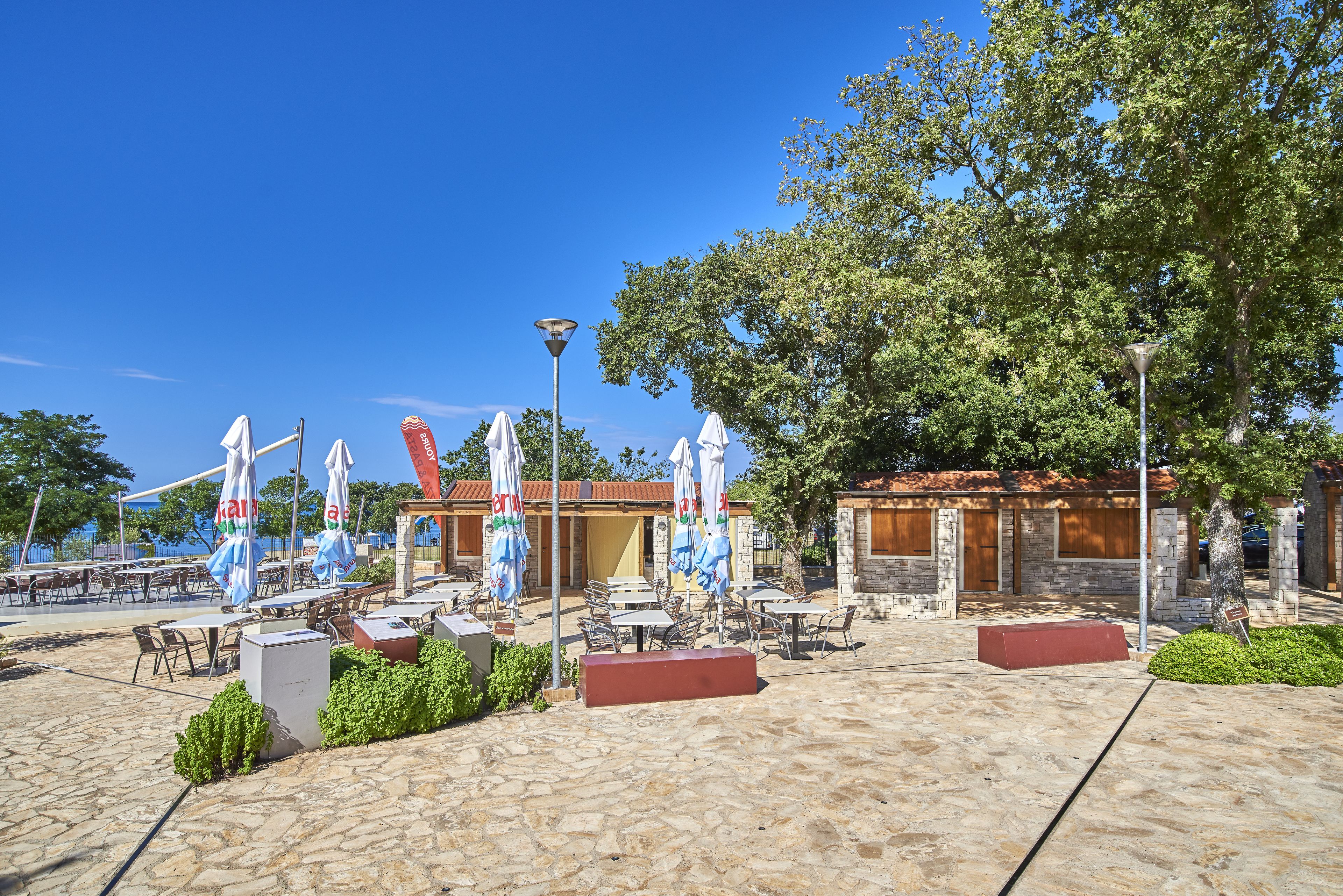 Un espace extérieur aménagé en terrasse, avec un sol en pierre, des tables, des chaises et des parasols.