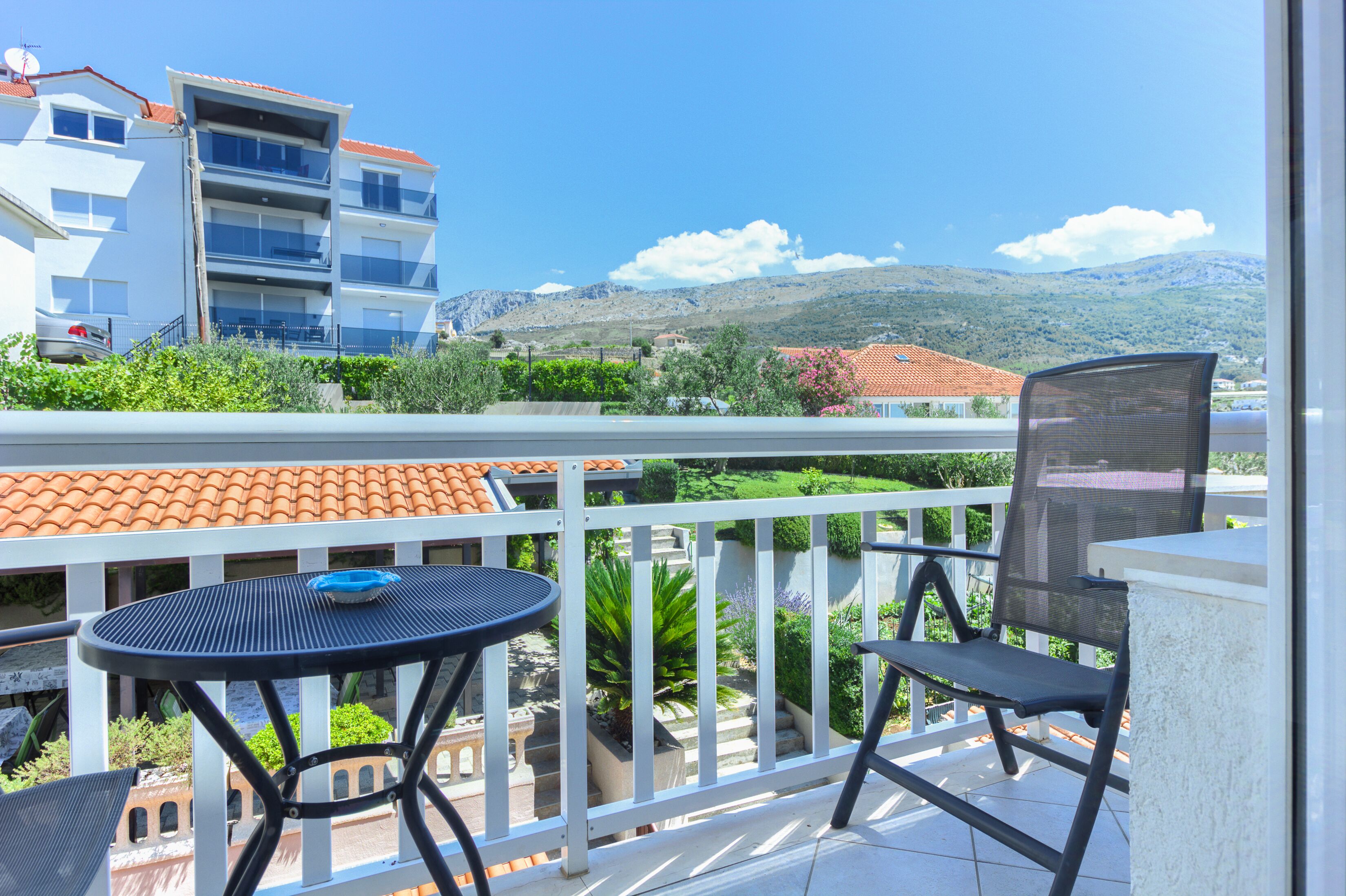 Ein Balkon mit Tisch und Stühlen mit Blick auf eine Berglandschaft und ein Gebäude mit roten Ziegeldächern.