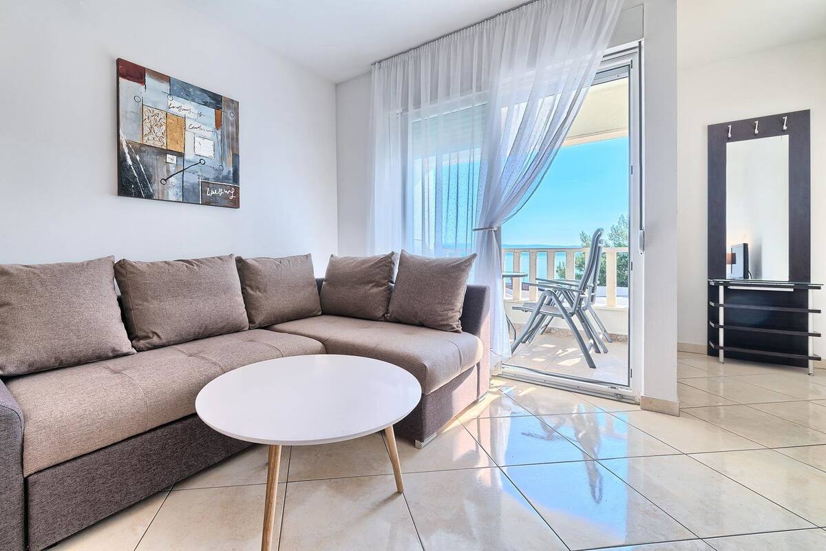 A modern living room with a beige sectional sofa, a white coffee table, and a large window with sheer curtains.