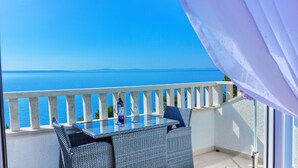 Ein Balkon mit Glastisch und Korbstühlen mit Blick auf ein Gewässer.