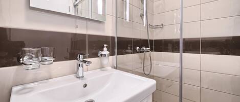 Une salle de bain moderne avec un lavabo blanc, une douche en verre et un miroir au-dessus du lavabo.