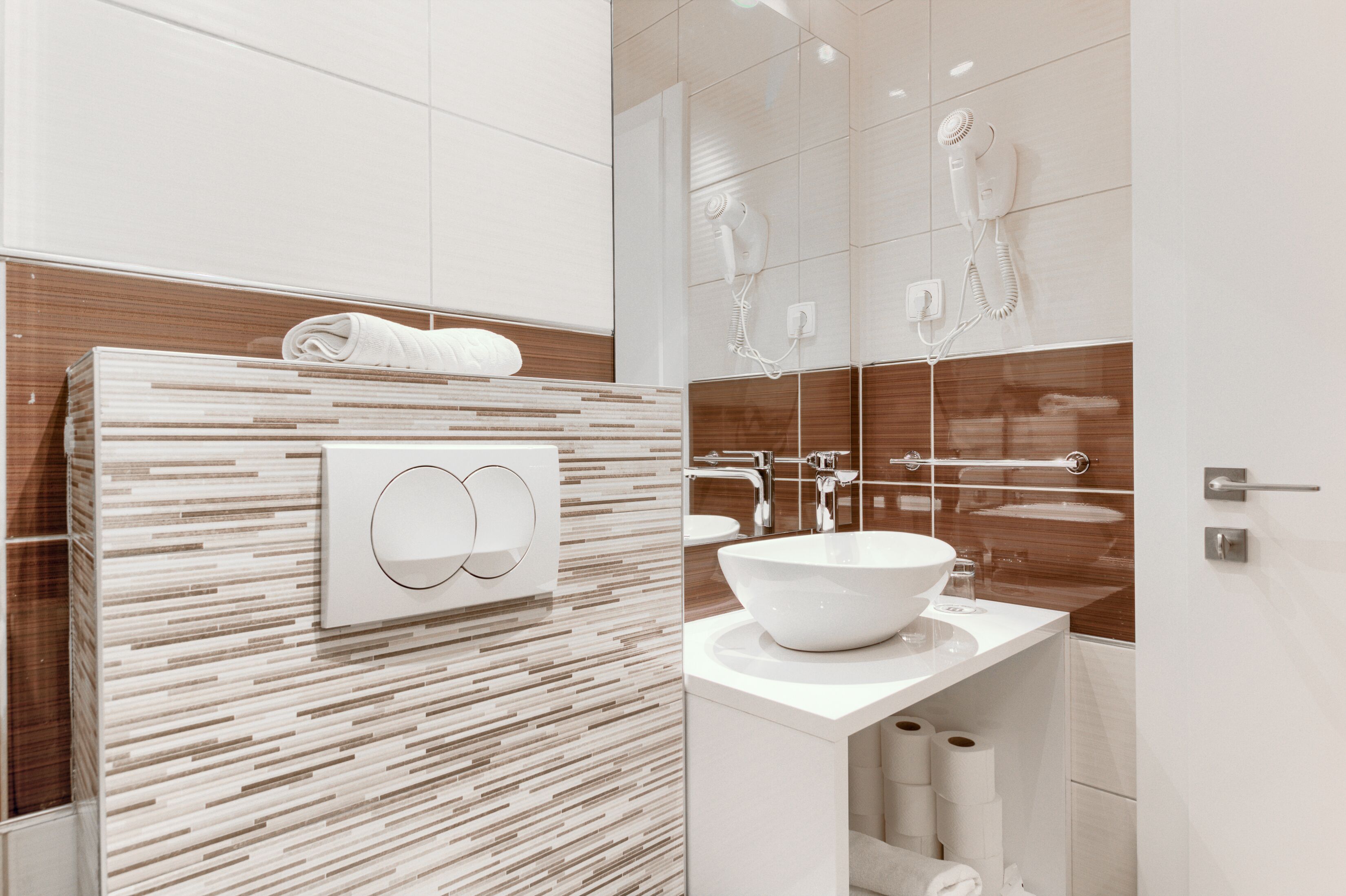A modern bathroom with a large mirror, a white sink, and a towel rack.