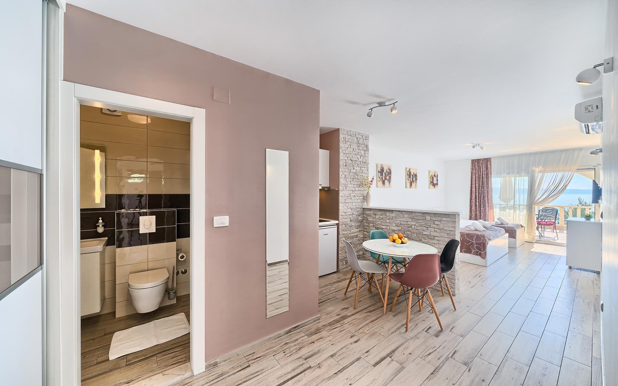 A modern hotel room with a dining area, a kitchen, and a balcony with a view.
