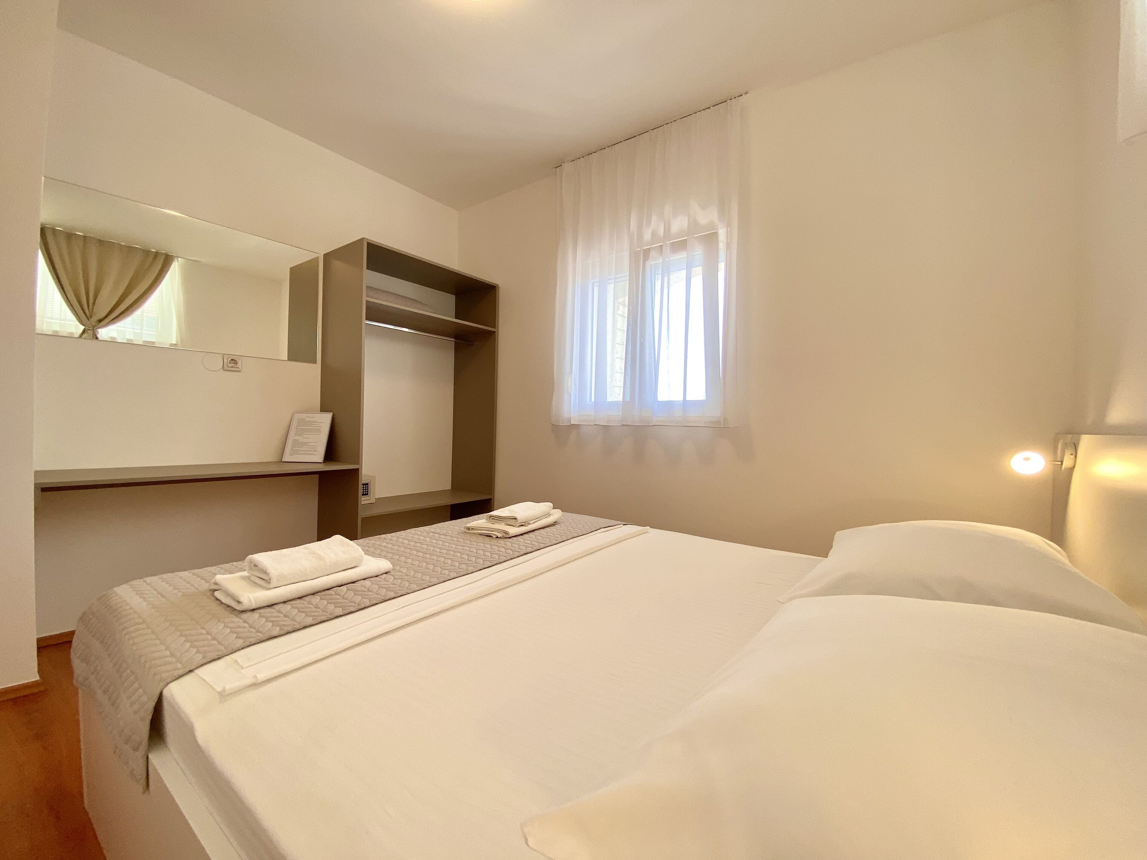 A hotel room with a bed, a bedside table, a mirror, a wardrobe, and a window with curtains.