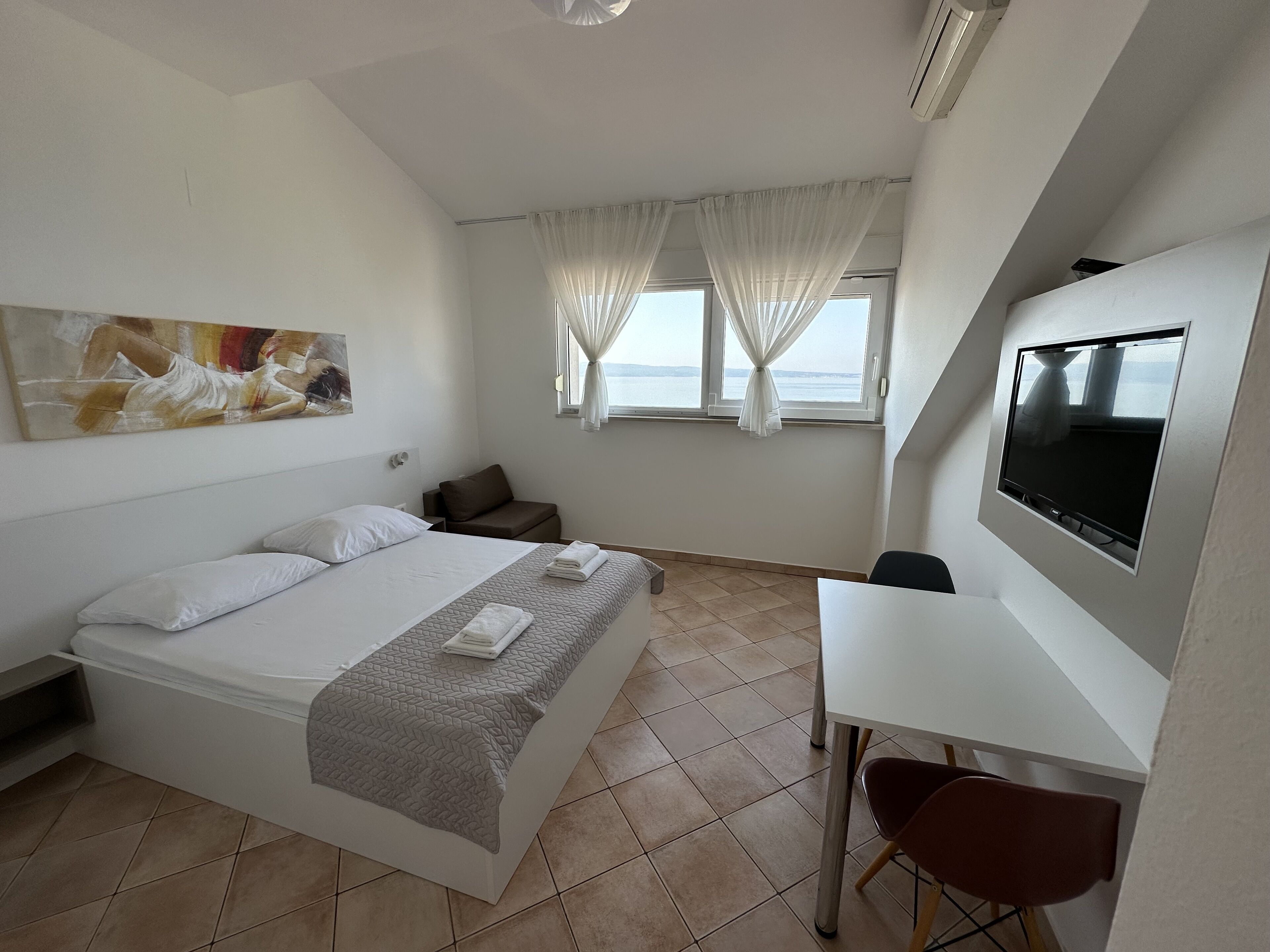 A hotel room with a bed, a desk, a TV, and a window with curtains.