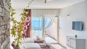 Ein modernes Hotelzimmer mit Steinwand, großem Fenster mit durchsichtigen Vorhängen, einem Bett mit weißer Bettwäsche und einem kleinen Schrank.