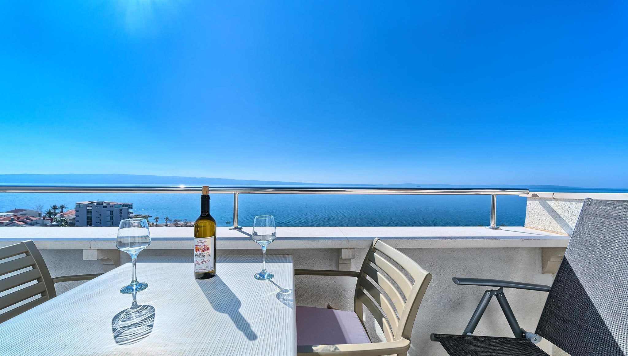 Een tafel met twee wijnglazen en een fles wijn, met uitzicht op de kust.