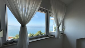 Ein Zimmer mit zwei großen Fenstern, weißen Vorhängen, einer Wandleuchte und Meerblick.