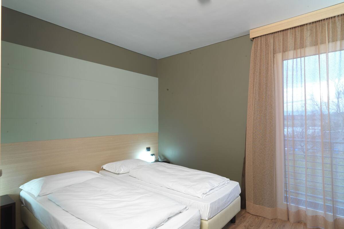 Una habitación de hotel con dos camas, una mesita de noche, una lámpara y una ventana con cortinas.