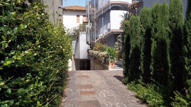 A narrow stone pathway flanked by lush greenery and modern buildings with balconies and potted plants. - Empoli Hotel (Empoli)