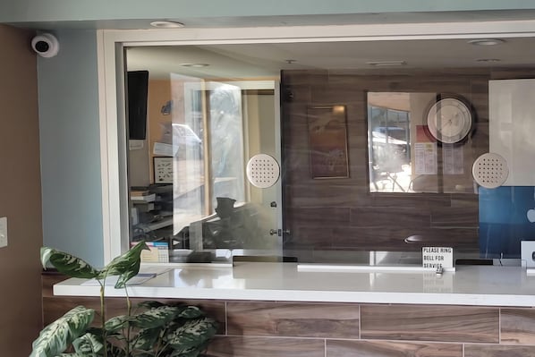 A reception desk with a glass partition, a clock, and a sign instructing to ring the bell for service.
