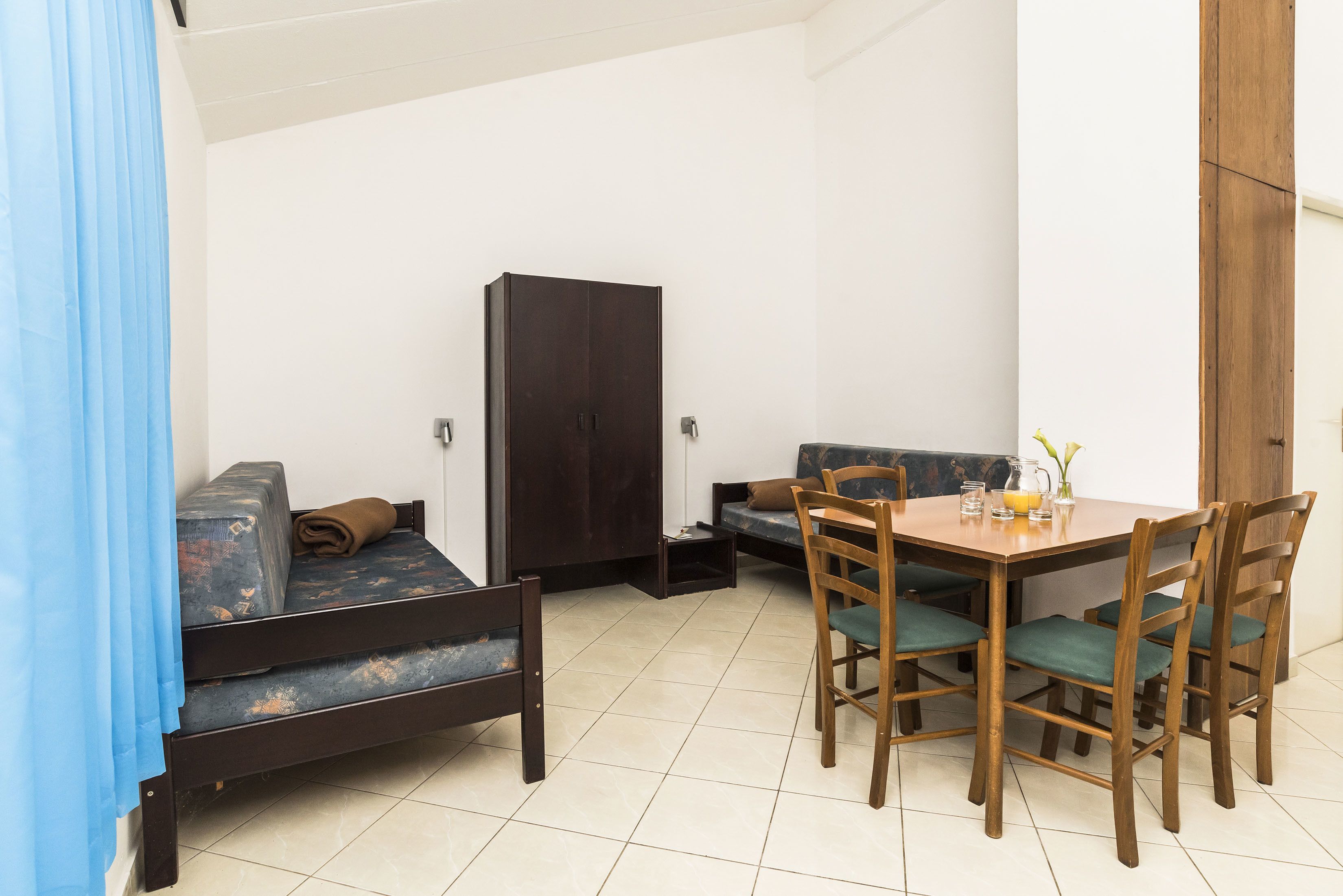 A compact room with a bed, a sofa, a dining table with chairs, and a wardrobe.