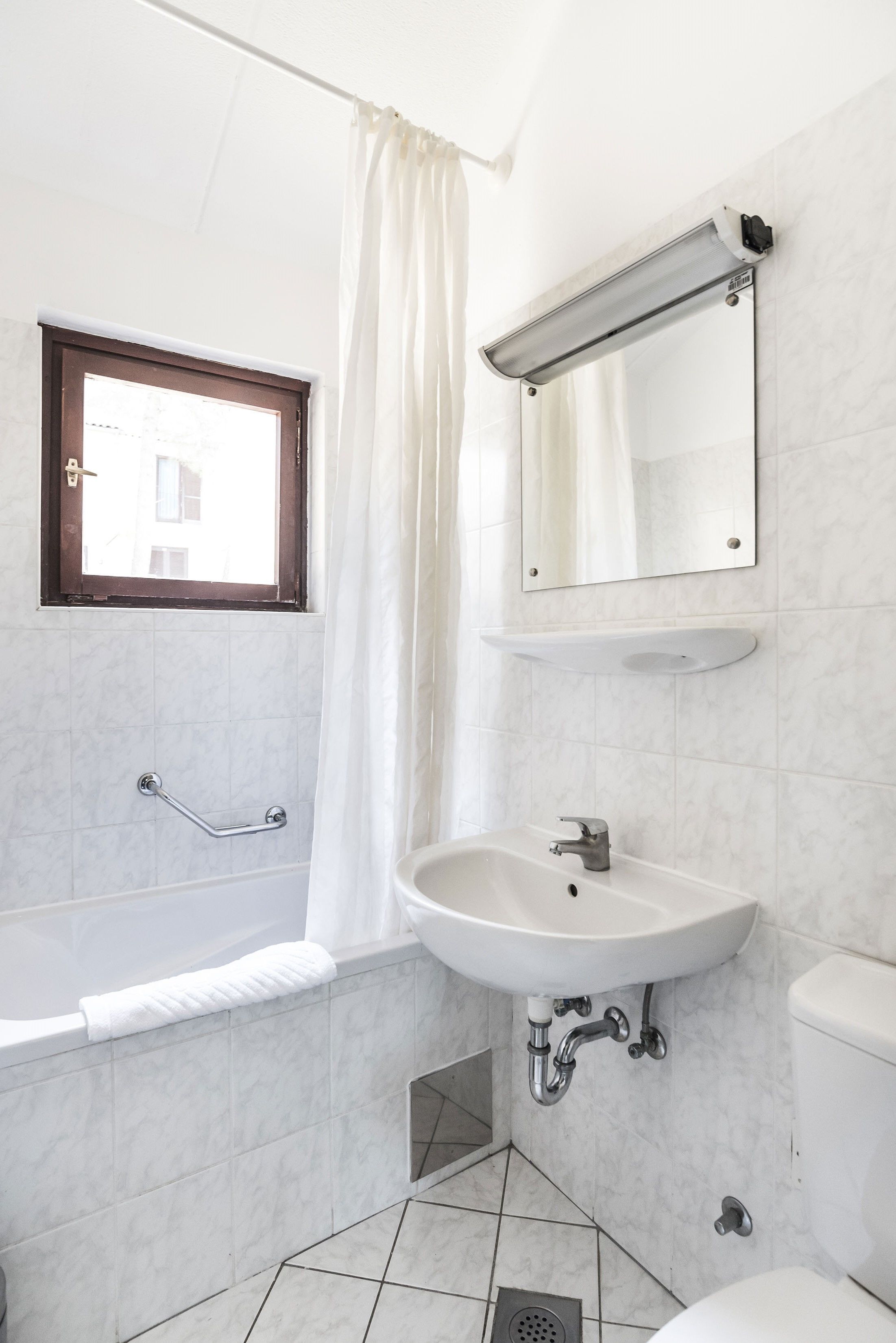 A bathroom with a bathtub, a sink, a toilet, a window with a curtain, and a mirror.