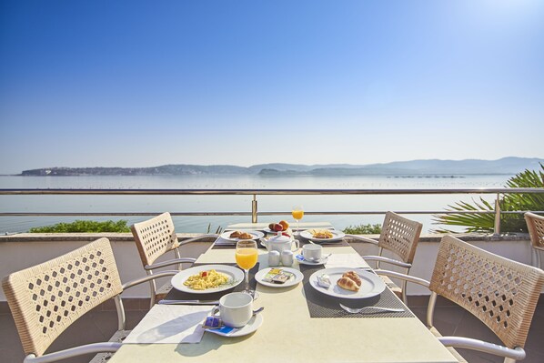 A table set for breakfast with a view of the sea and mountains.