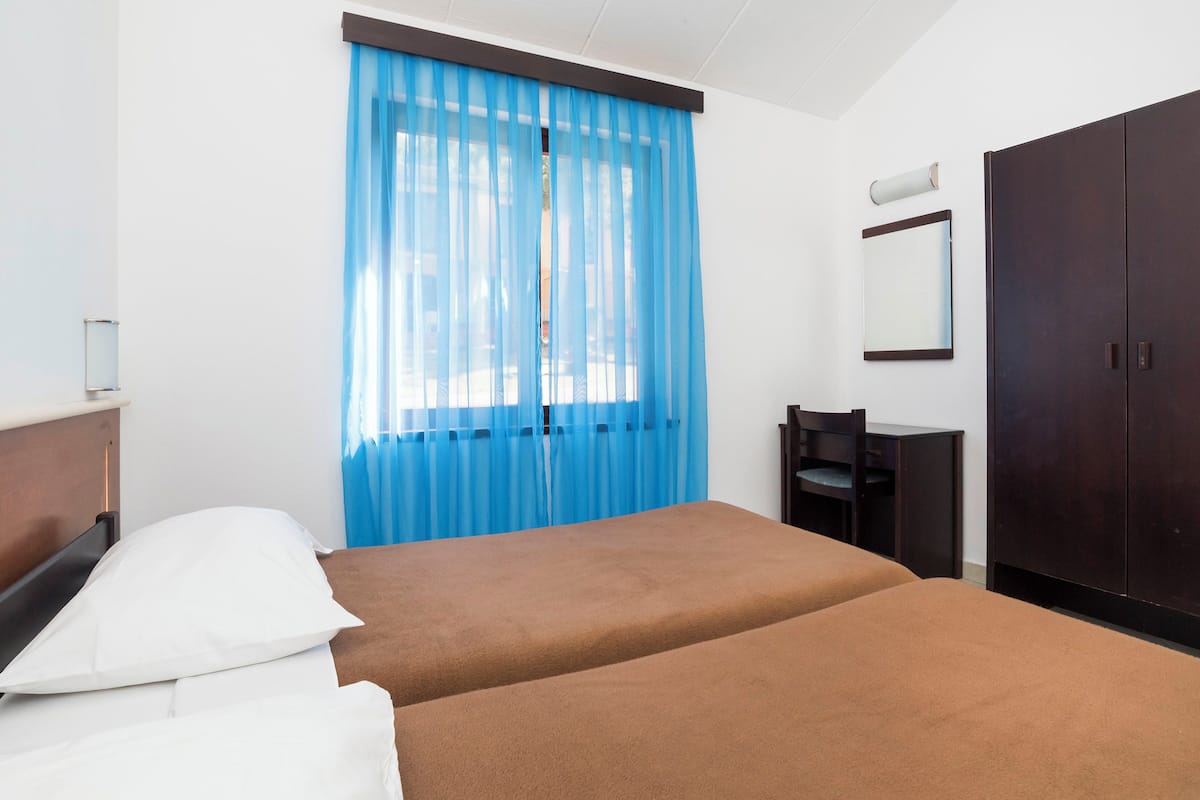 Ett hotellrum med två sängar, ett skrivbord, en stol, en garderob och ett fönster med blå gardiner.