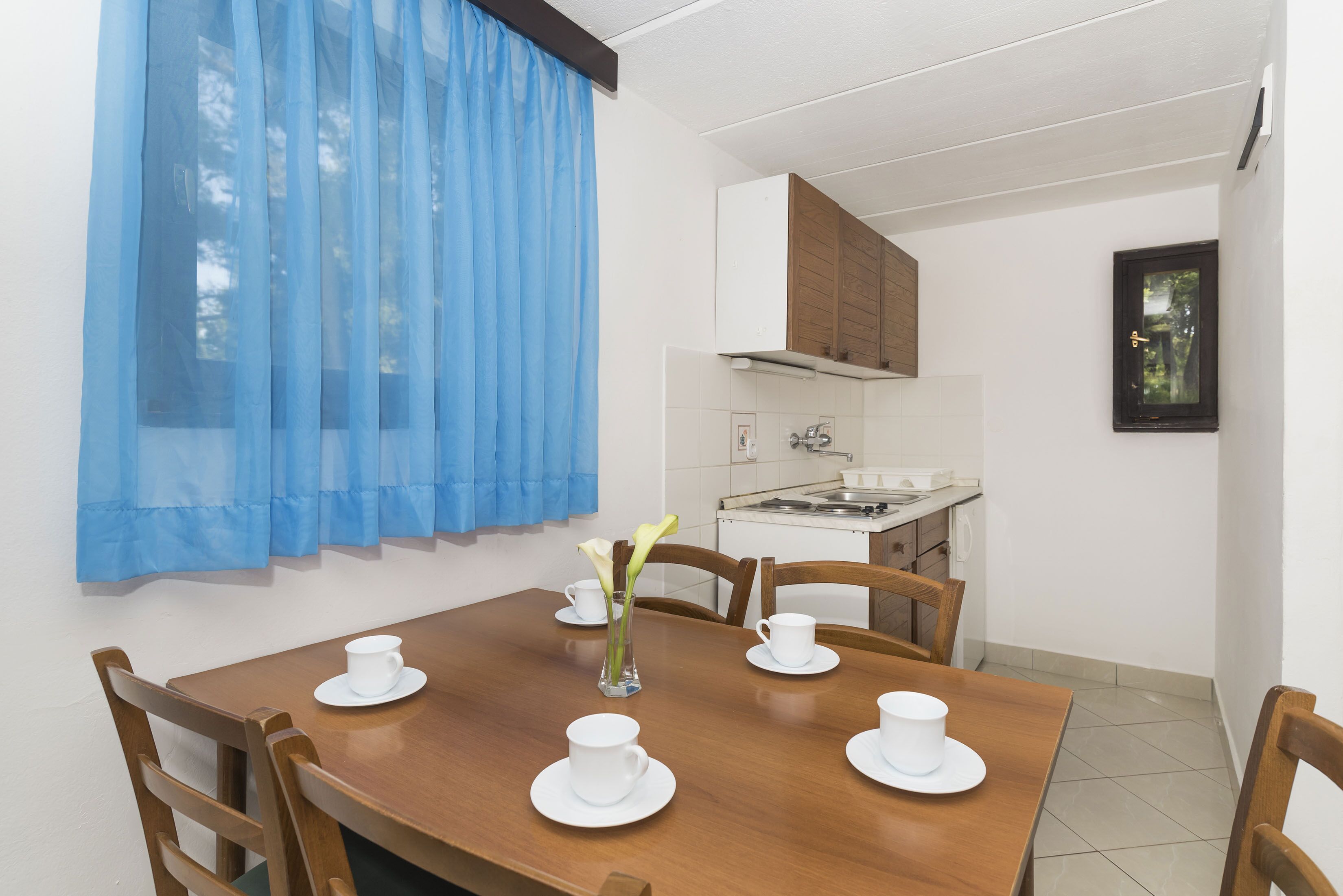 Un comedor con una mesa de madera, tazas blancas y un jarrón con flores.