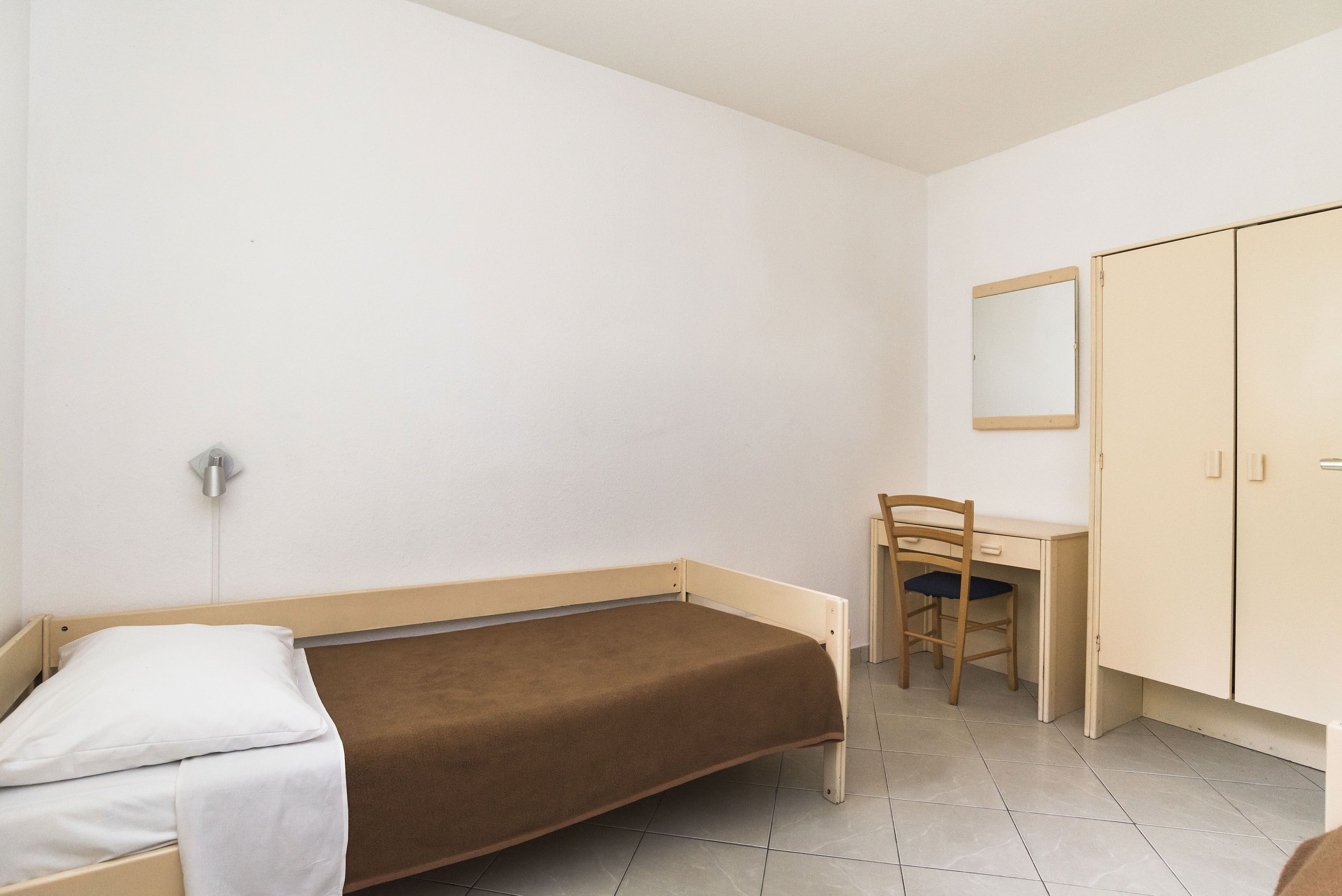 Un lit simple avec un matelas marron, un bureau en bois avec une chaise et une armoire.