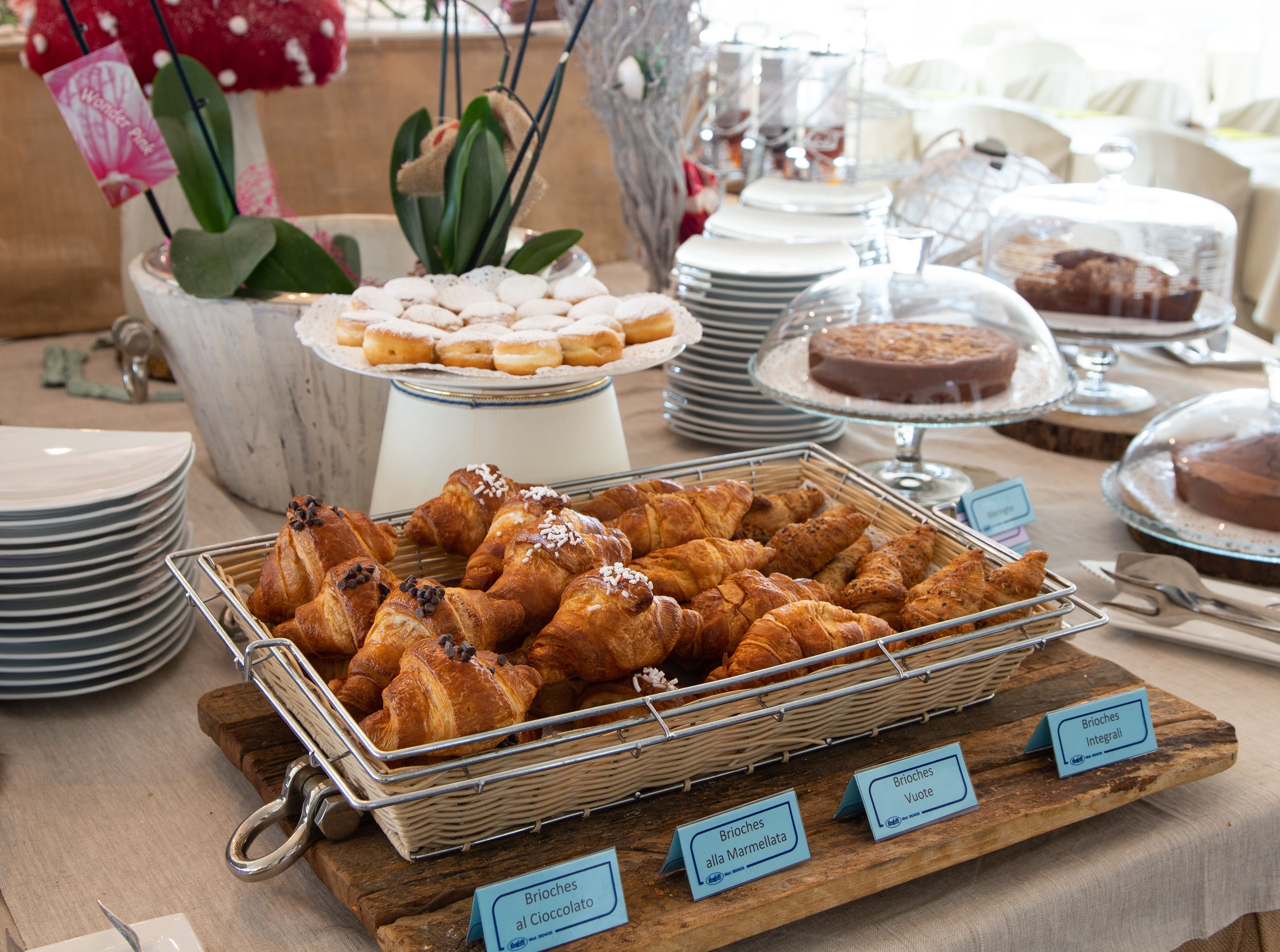 Un tavolo del buffet con diversi prodotti da forno, tra cui croissant e torte, con le relative etichette.
