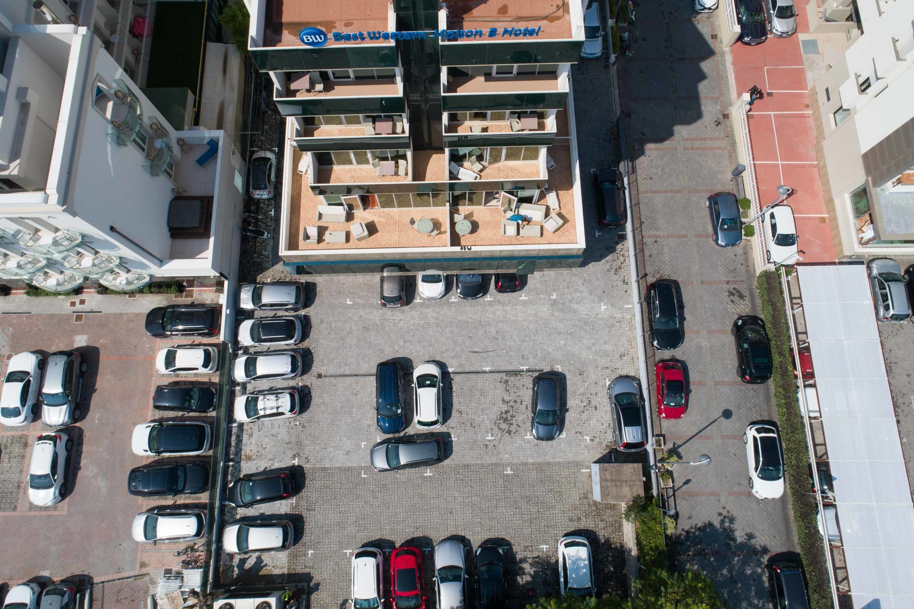 An aerial view of a hotel with a rooftop terrace, multiple parking spaces, and a multi-story building.