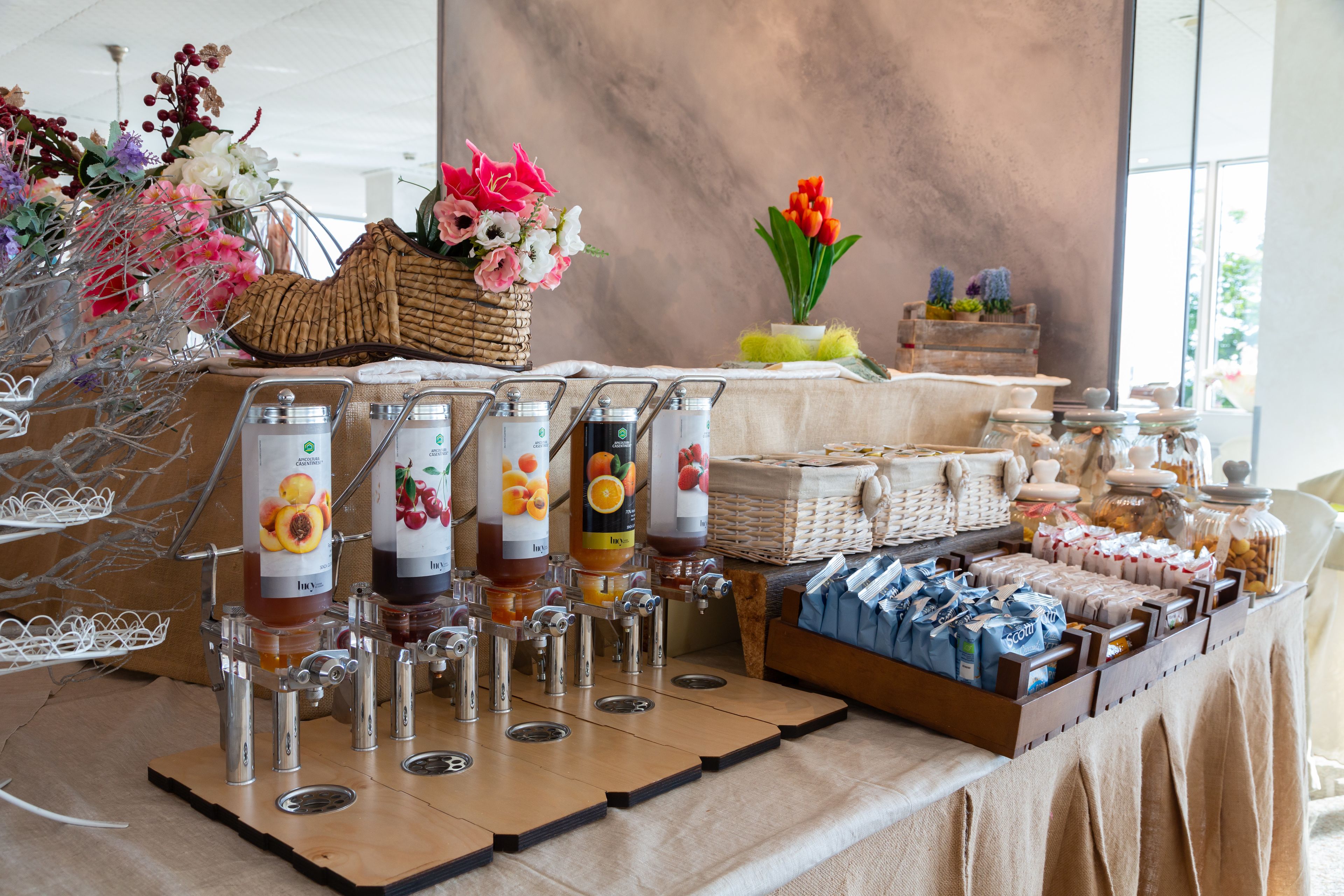 Una mesa de buffet con diversos alimentos y bebidas, incluyendo frascos de mermelada y botellas de jugo.