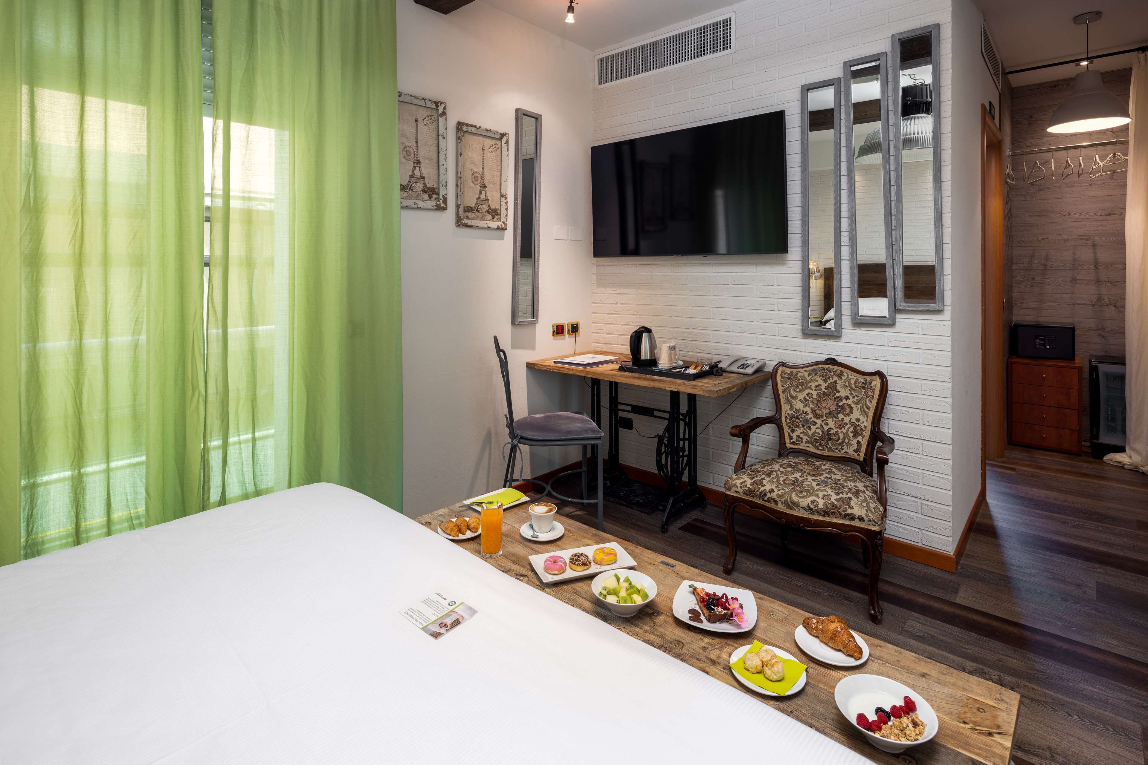 Een hotelkamer met een bed, een ontbijttafel met diverse gerechten, een bureau met stoel, een televisie en een raam met gordijnen.