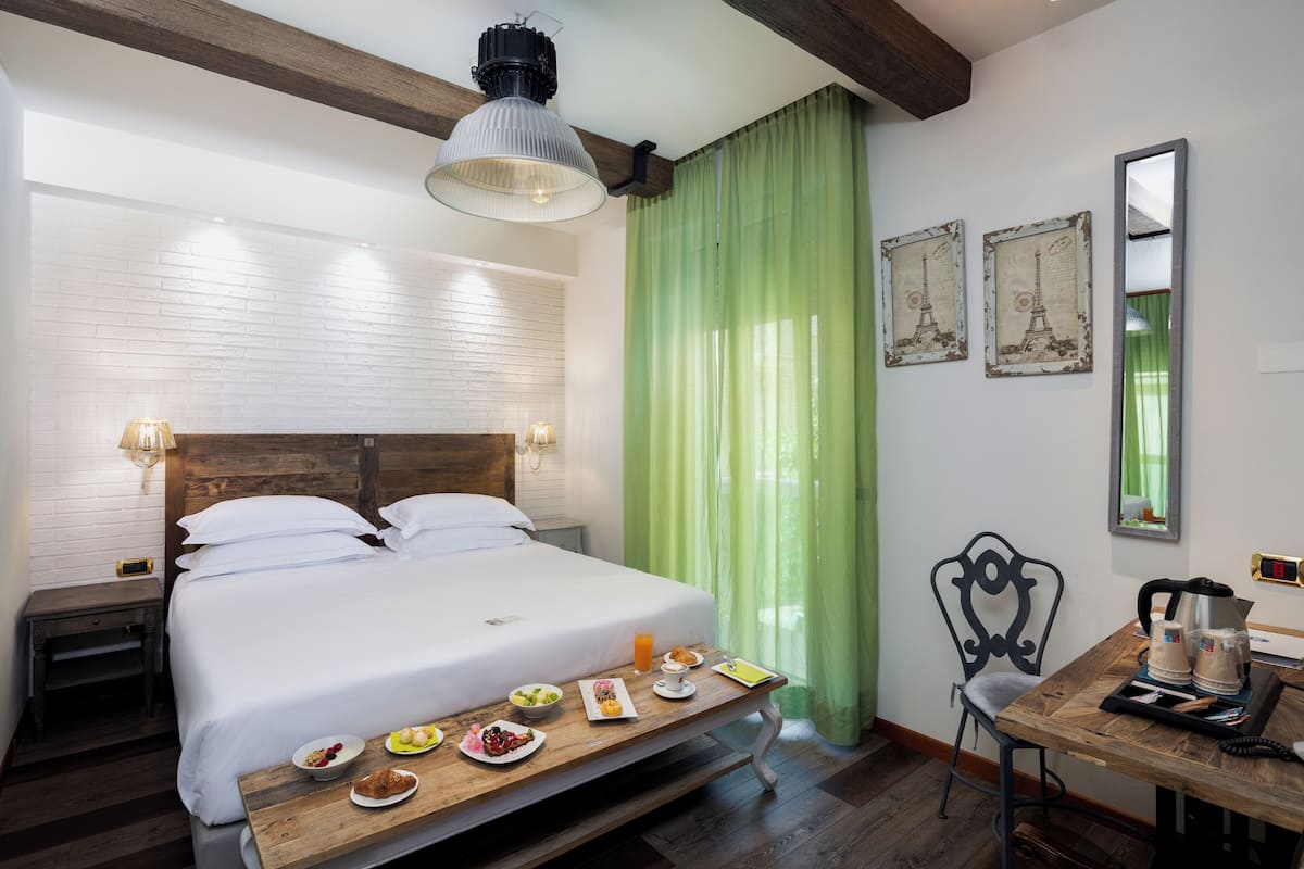 A hotel room with a wooden bed, a breakfast trolley, a coffee maker, and a chair.