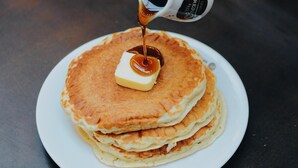 Una pila de tortitas en un plato blanco con jarabe que se está vertiendo encima.
