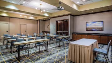 A conference room with tables, chairs, a projector, and a painting on the wall.