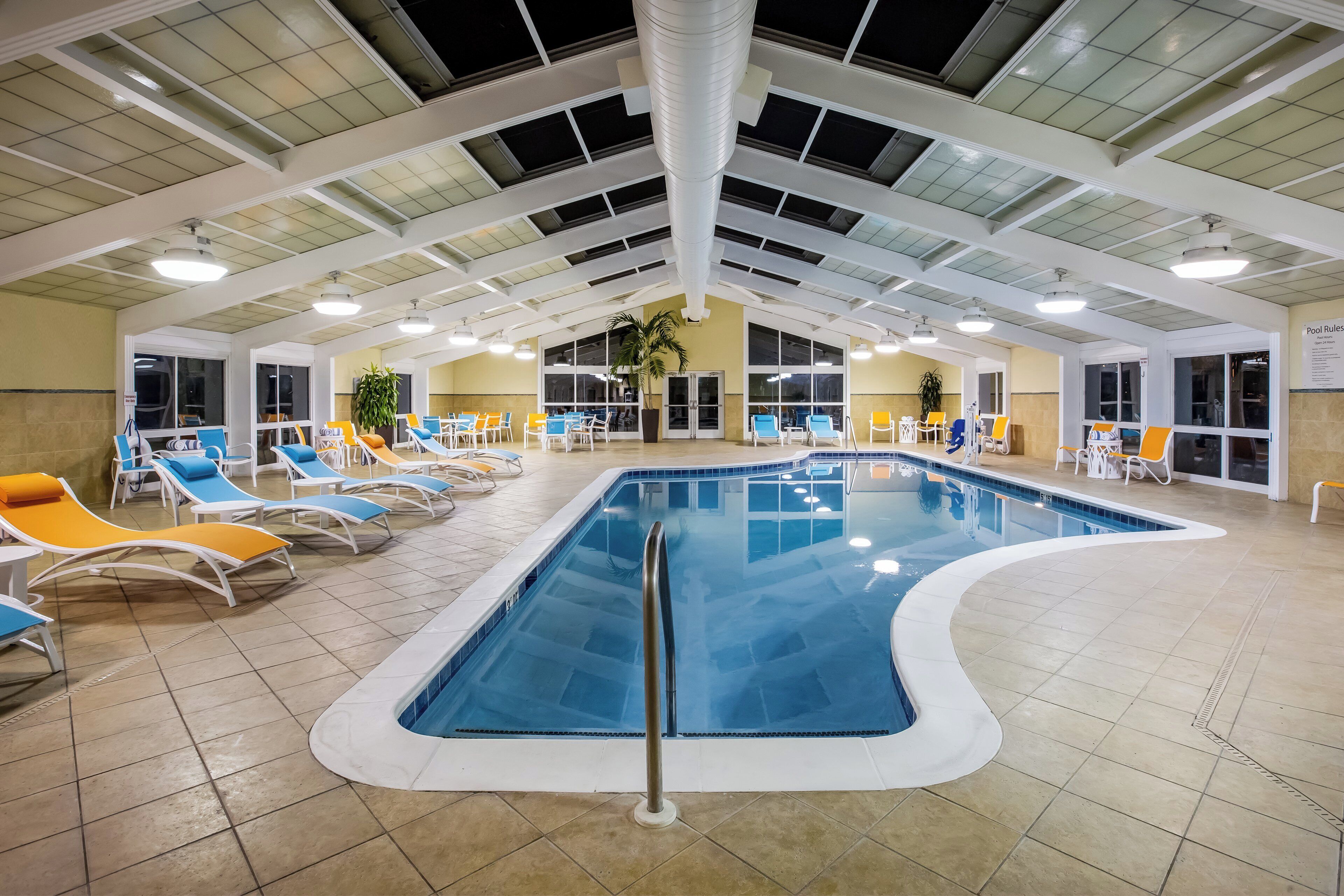 Ein Hallenbad mit mehreren Bahnen, umgeben von Liegestühlen und einer hohen Decke mit Oberlichtern.