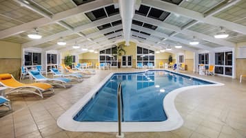 Ein Hallenbad mit mehreren Bahnen, umgeben von Liegestühlen und einer hohen Decke mit Oberlichtern.
