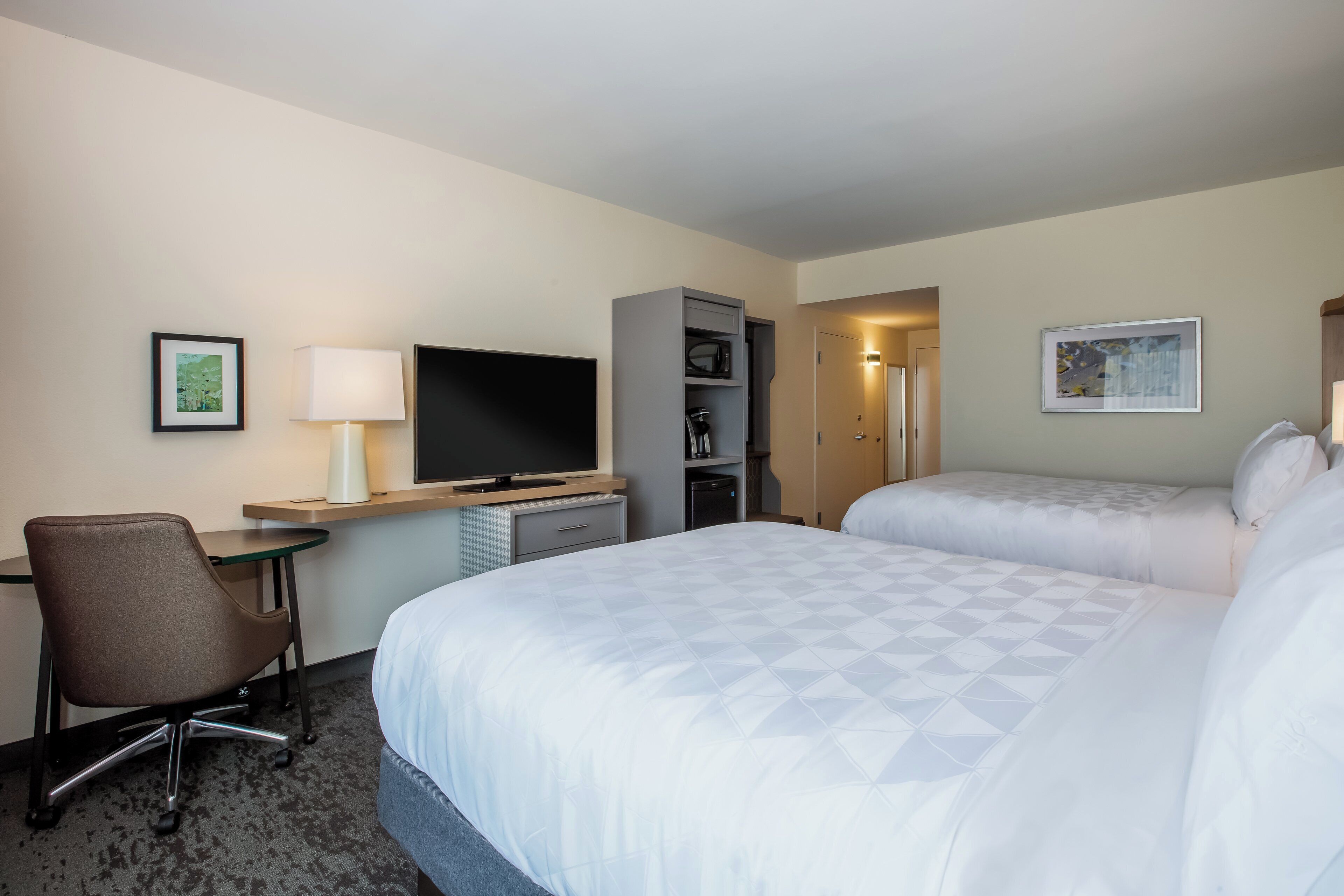 A hotel room with a bed, a desk with a TV, a chair, a wardrobe, and a door leading to another room.