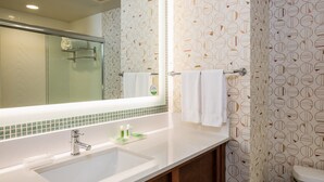 Un baño con un espejo grande, un lavabo con artículos de aseo y un papel tapiz estampado.