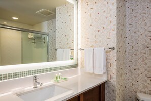 A bathroom with a large mirror, a sink with toiletries, and patterned wallpaper. - Holiday Inn Gulfport Airport by IHG (Gulfport)