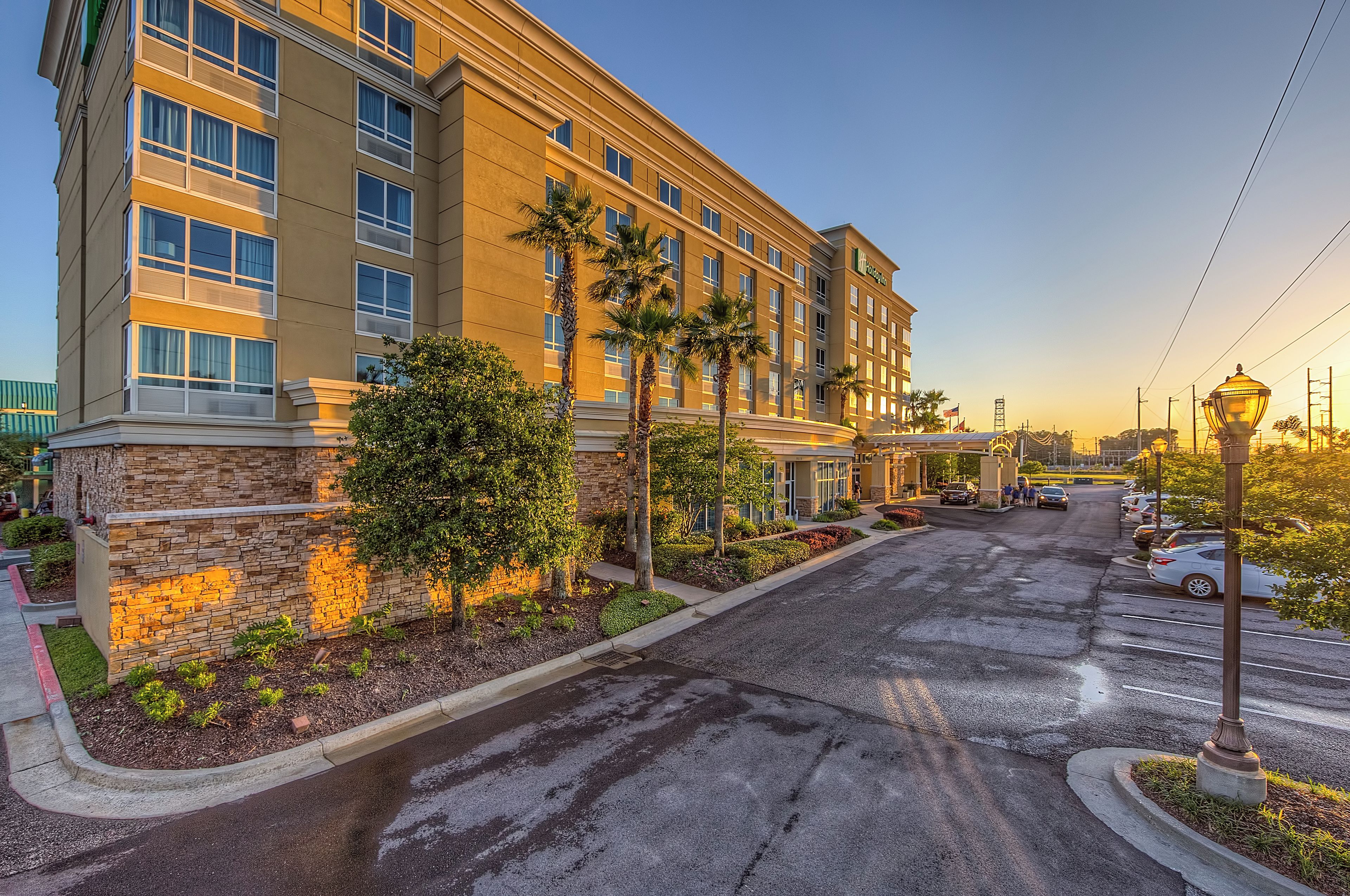 A multi-story hotel with a stone facade, palm trees, and a parking area.