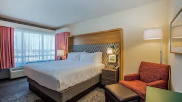 A hotel room with a large bed, a chair, a small table, a nightstand, and a lamp.