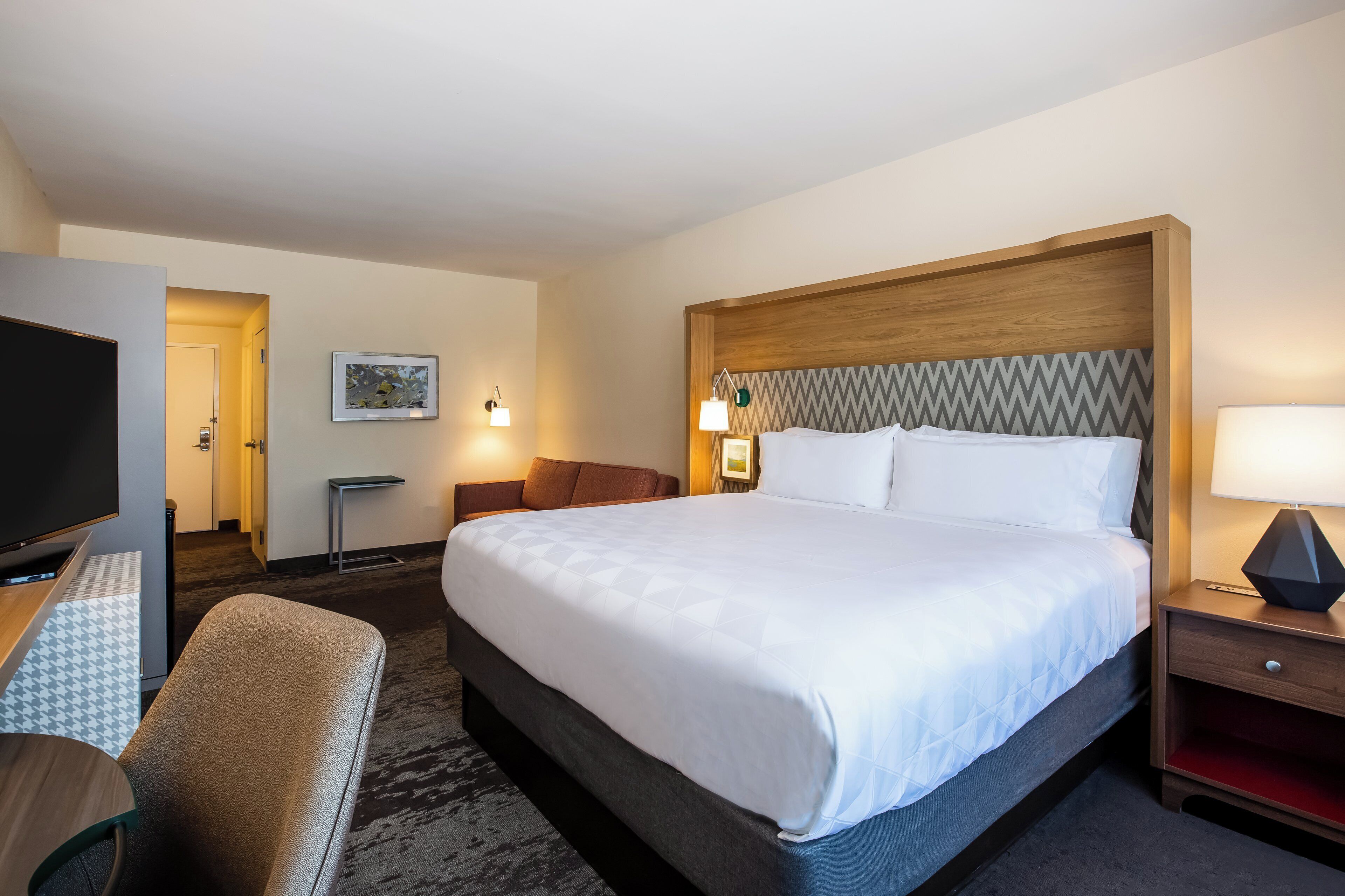 A hotel room with a large bed, a TV, a desk, and a chair.