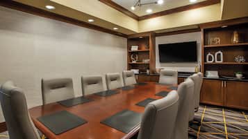A conference room with a large table, six chairs, a television, and shelves with decorative items.