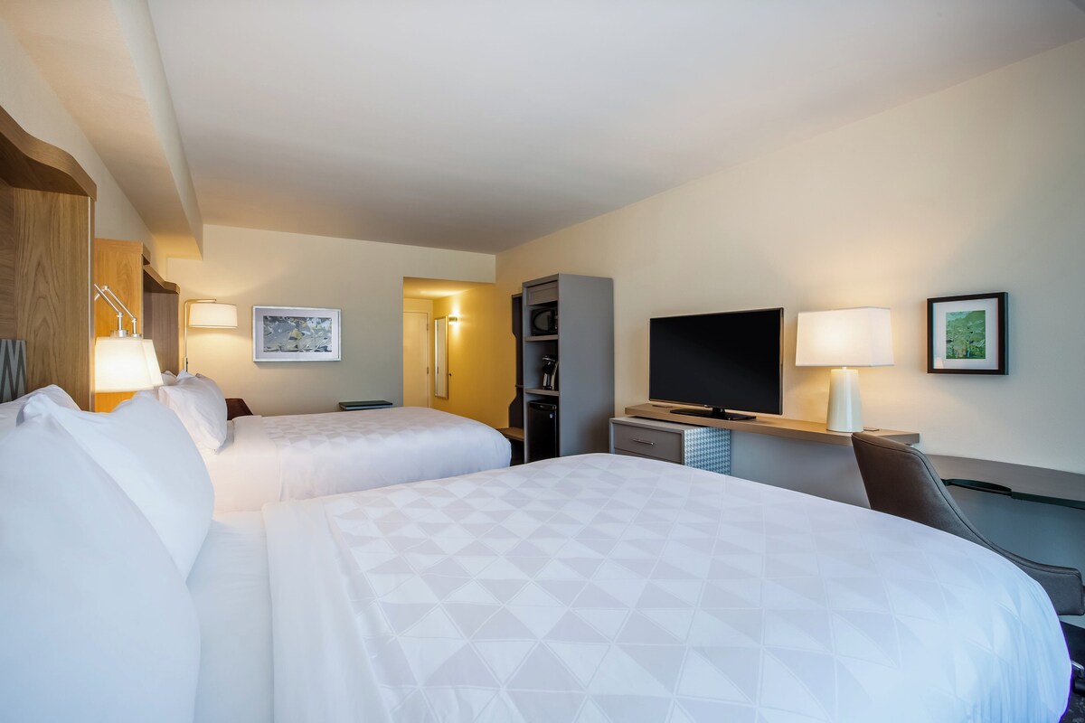 A hotel room with two beds, a TV, a desk, and a chair.