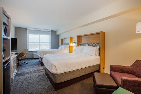 A hotel room with two beds, a desk, a chair, a TV, and a view of the city. - Holiday Inn Gulfport Airport by IHG (Gulfport)