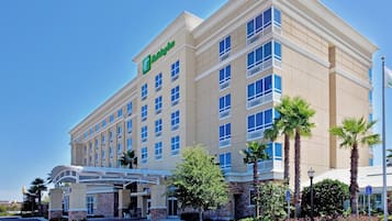 Un hotel Holiday Inn con cielo sereno, ingresso coperto e palme.