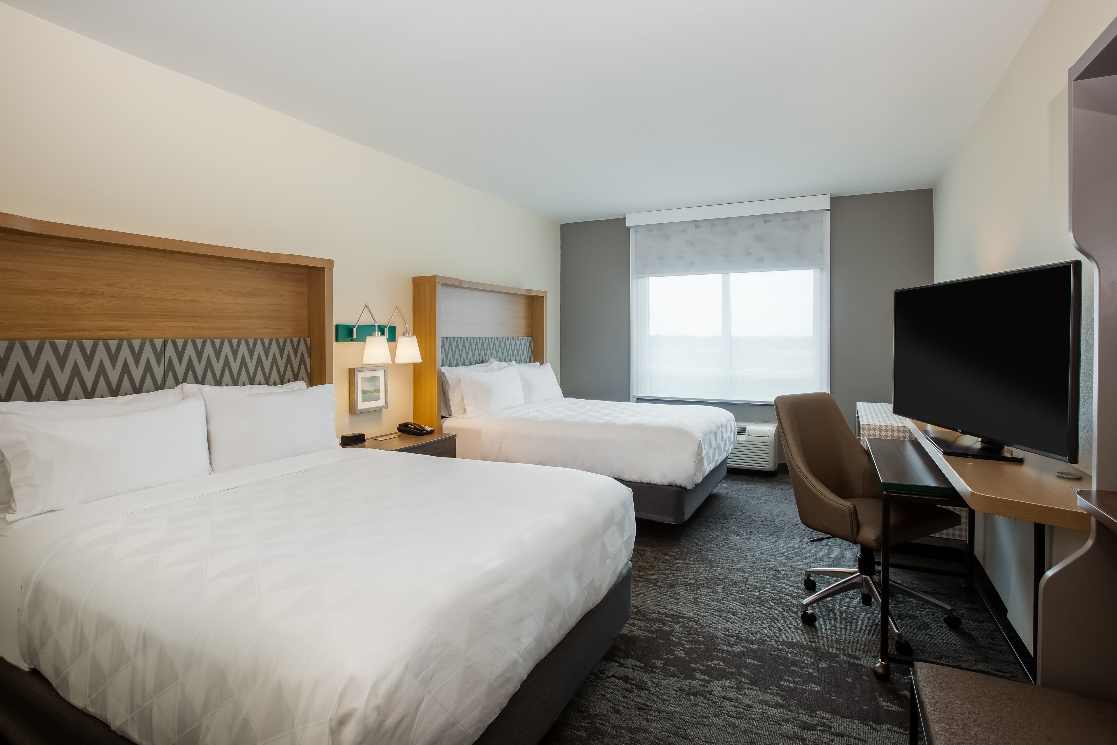 A hotel room with two beds, a desk, a television, and a window.