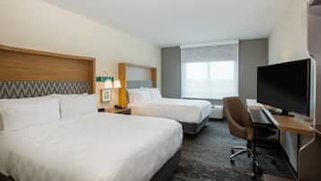 A hotel room with two beds, a desk, a television, and a window.